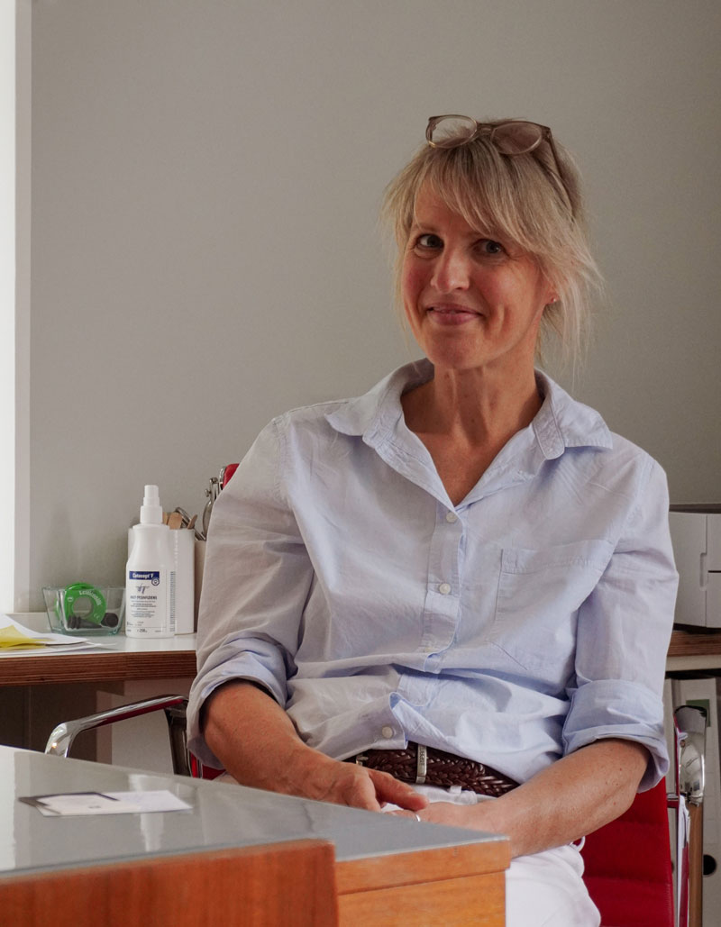 Dr. C. Walliser, Ärztin für Allgemeinmedizin, freundlich in die Kamera schauend, am Schreibtisch sitzend